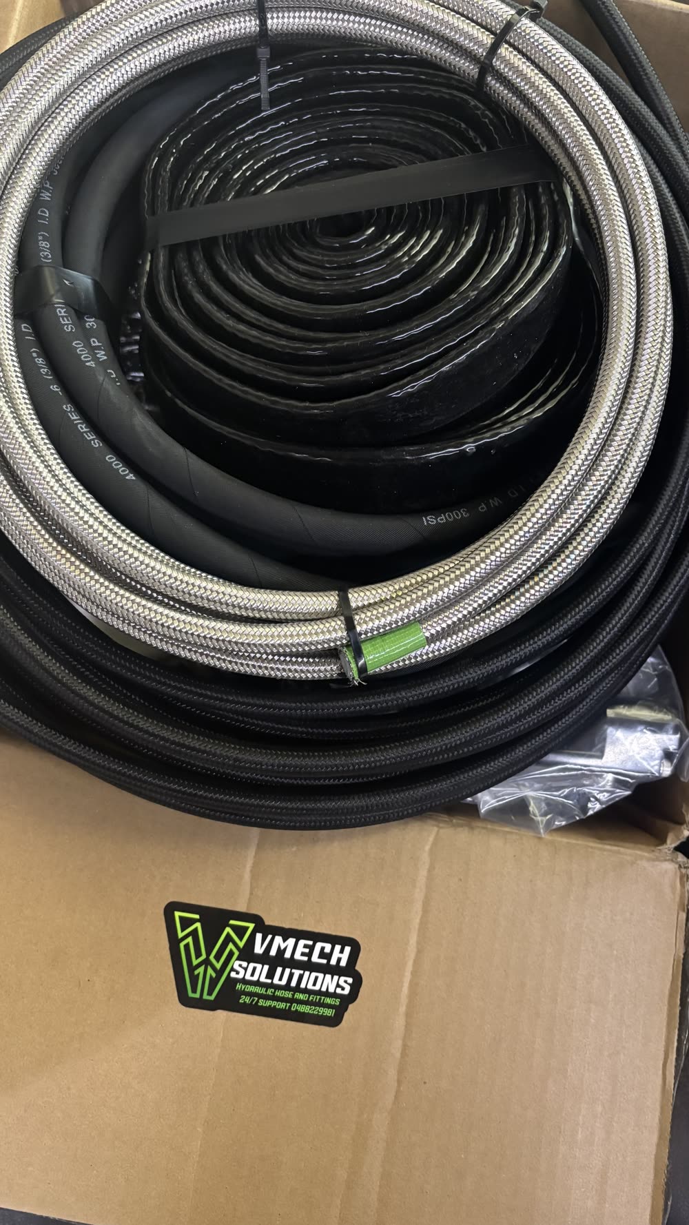 Box of stainless braided and rubber performance hose coils with a VMECH Solutions sticker